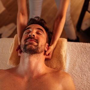 Close up shot of a young man with a beard enjoying a head massage at a spa