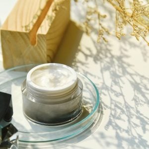 Skin care facial cream in container with shadow of leaves alongside.