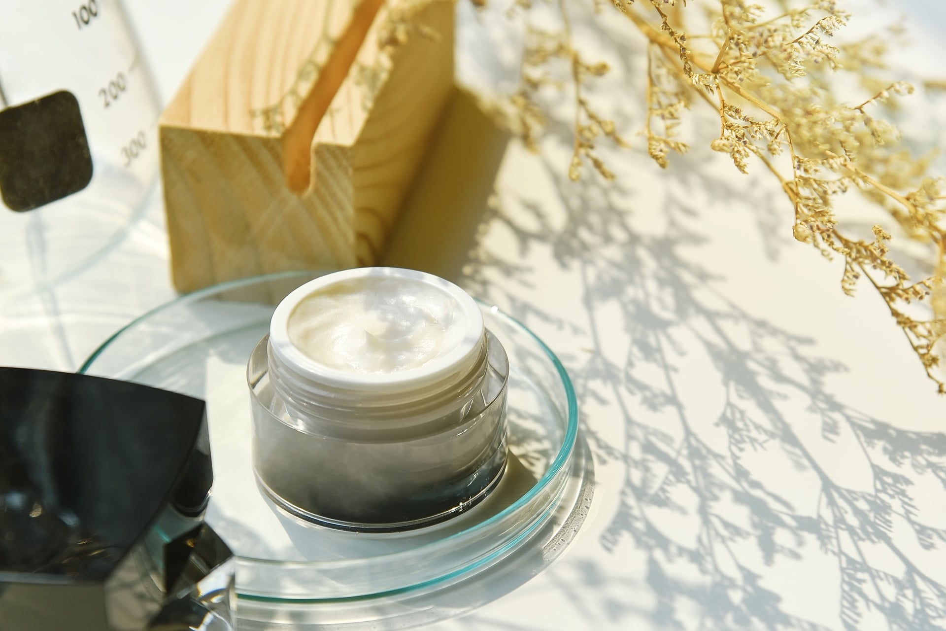 Skin care facial cream in container with shadow of leaves alongside.