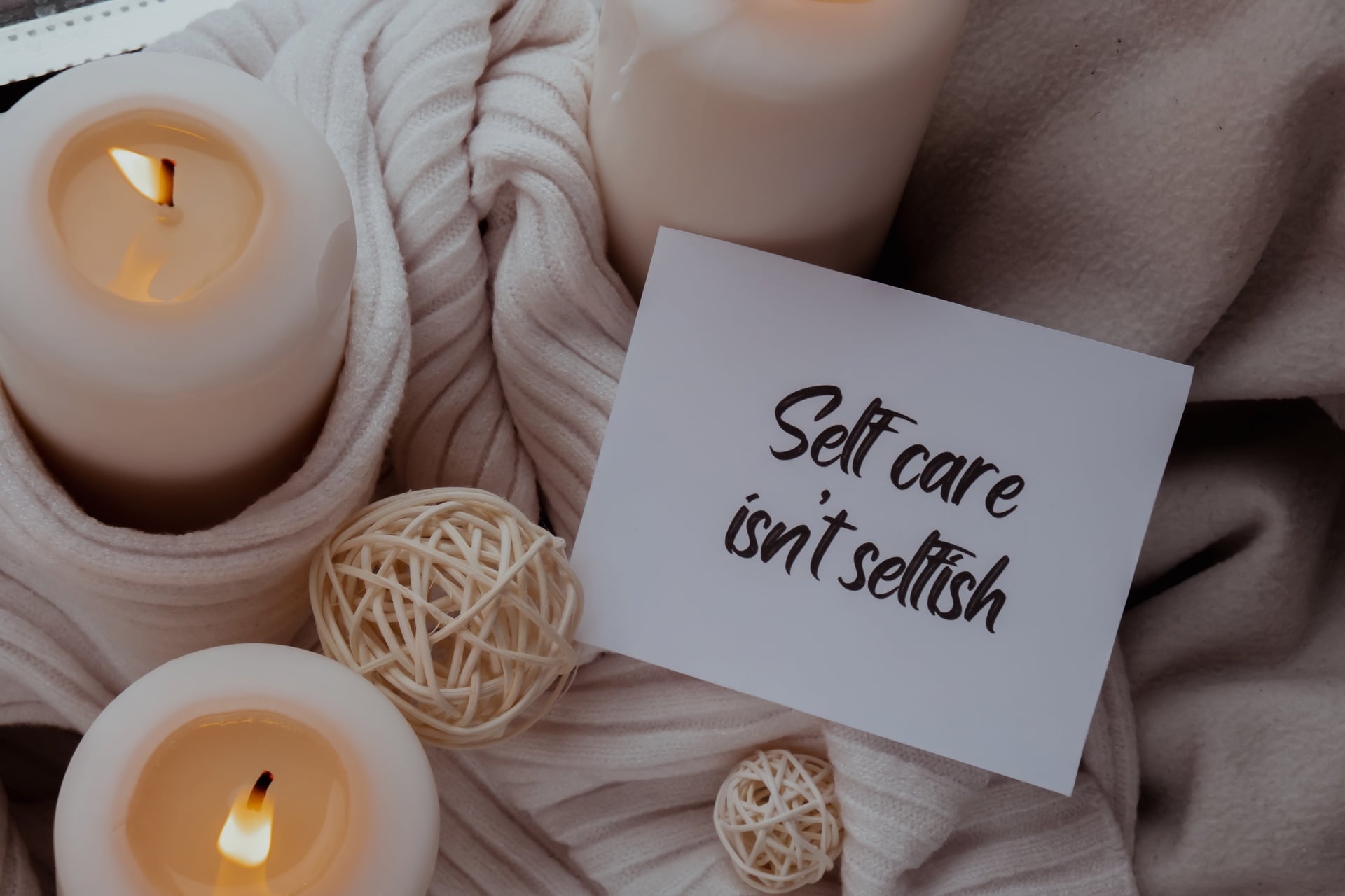 SELF CARE ISNT SELFISH text saying phrase on paper note on background of scented candles.